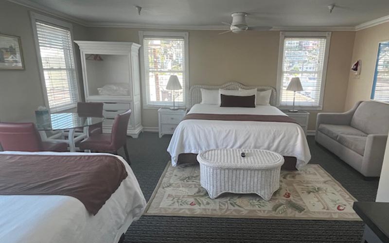 Hotel room with two beds, a wicker coffee table, and a sofa in a sunlit suite.